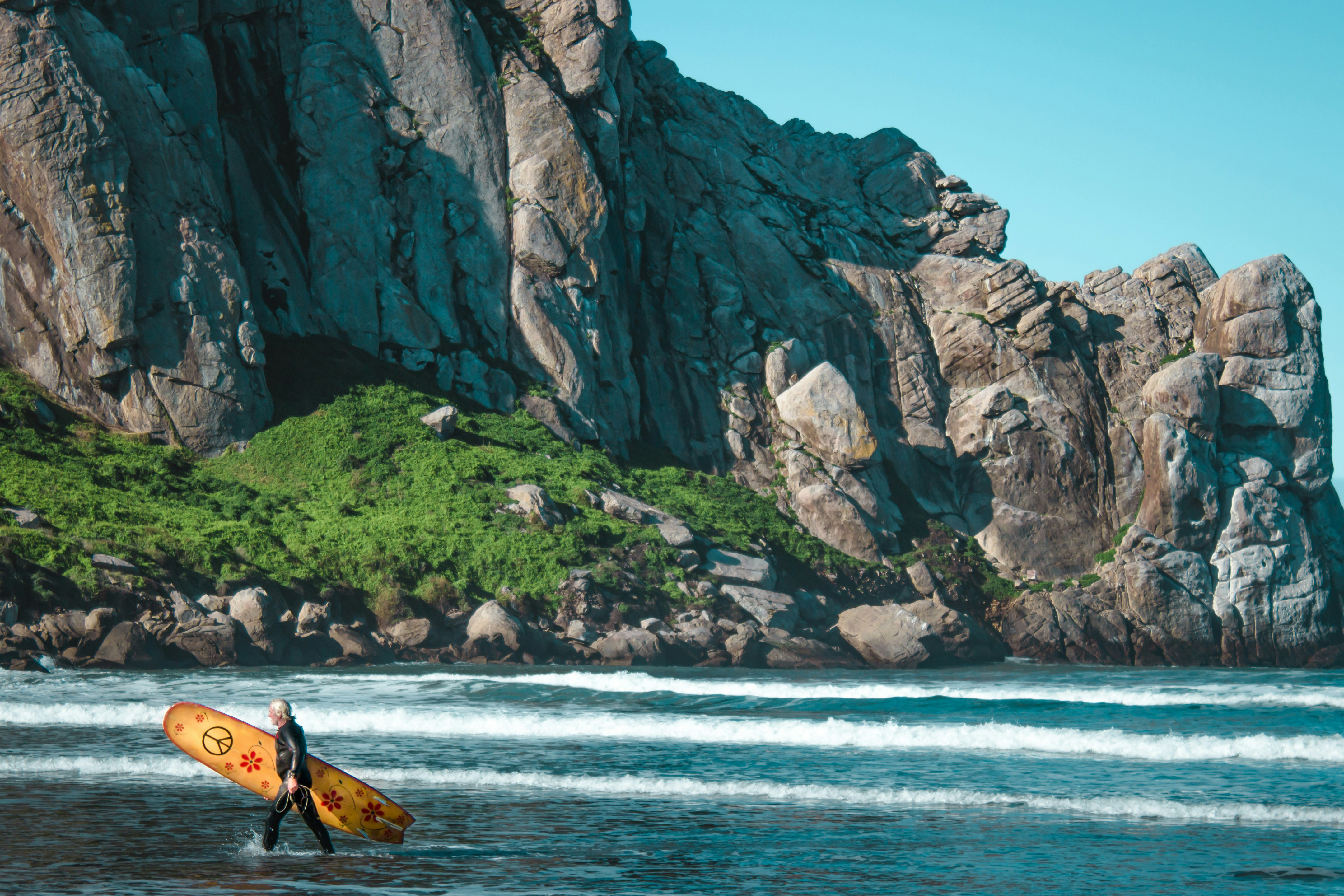 man walking with surfboard in front of morro rock.